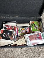 Box containing a large collection of mixed sports trading cards mostly basketball and football, stored loosely with many card stacks visible in different colors and designs.