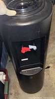 Front view of black water cooler dispenser showing red and white water taps and drip tray.