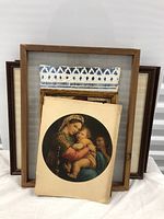 Five art pieces arranged with religious print featuring Madonna and child centered and closest, backed by a gold-framed portrait and other framed artworks.