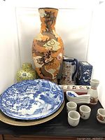 Full assortment of Asian pottery items showing large dragon vase, yellow ginger jar, pitcher, plates, sake set, soup spoons, and incense burner box.
