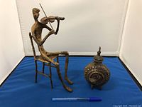 Wide shot showing the brass violin player figurine next to the antique ink well with a pen for size reference