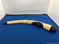 Side view of curved bone pipe showing detailed Chinese carvings and black mouthpiece.