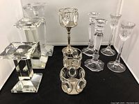 Seven candlesticks including clear crystal and silver tone metal prism holders shown on black and white surfaces