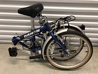 Folded blue Dahon Mariner folding bicycle with rear rack, pedal, and tires visible