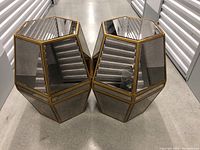 Pair of hexagonal beveled mirrored drum tables side by side on concrete floor in storage unit.