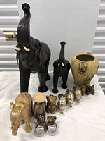 Overall grouping showing two large dark brown elephants in back, beige vase at right, and assortment of smaller figurines in front