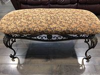 Front view of the upholstered foyer bench with wrought iron frame on dark wood floor.