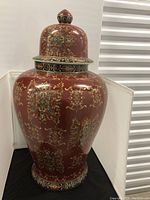 Full view of the large ceramic ginger jar urn showing its body and lid with detailed gold and green ornamental floral designs on reddish-brown base.