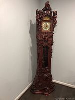 Full-height front view of carved wooden clock in corner against gray walls.