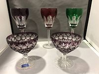 Front view of three colored Hungarian stemware wine glasses and two champagne coupes with cut glass detailing on white background
