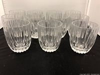 Image showing 11 clear lead crystal rocks glasses arranged in groups on a black surface, displaying the vertical fluted cut design and starburst bases.