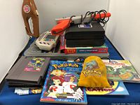 Photo showing the full lot contents including the Nintendo Zapper, NES game cartridges, Pokémon marbles pouch, Pokémon books, vintage Pocket Fisherman, Battleship and Wheel of Fortune board games, Smithsonian Planetary Game, and handheld electronic game device.