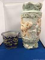Photo showing both the Dorothy ceramic umbrella stand with detailed raised figure designs and the blue and yellow Italian ceramic flower pot side by side.