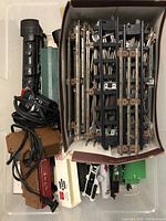 Top view of black O scale locomotive body, multiple train tracks neatly stacked, transformers and cords to the left.