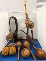 Wide shot showing entire lot including tall giraffe figurine, carved mask, deer and bird figurines, wooden maracas, Dutch shoes, and small cup.