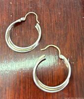 Pair of intertwined 10K gold and silver wire hoop earrings laid flat on a wooden surface, showing complete view of hoops and clasps.