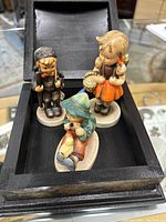Three vintage Goebel Hummel porcelain figurines displayed in a wooden box.