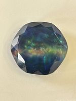 Faceted round ammolite gemstone showing iridescent colors and natural inclusions on a light background.