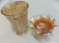 Photo showing a translucent amber depression glass vase with geometric pattern alongside an iridescent ruffled candy dish on a pedestal base.