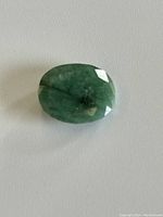 Oval cut emerald gemstone showing faceted surface, medium to dark green with natural inclusions.