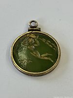 Front view of the pendant showing round green jade with carved figure design set in gold fill frame.