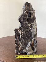 Front angled view of granite sculpture standing on table with tape measure showing height approximately 6 inches. The time machine encased in a transparent cylinder is visible embedded into the granite base.