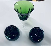 Top view of two green art glass mustard dishes with lids and a matching wine glass, showing shape and color.