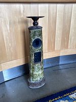 Side view of vintage metal pedestal showing textured green surface, square front detail, circular recessed feature, and round ridged base