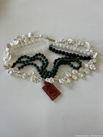 Full view of three necklaces laid out, including pearl necklaces with irregular shaped pearls, green malachite bead necklace, and a carnelian pendant attached.