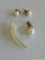 Photo of pearl stud earrings, white horn-shaped pendant, and pearl teardrop pendant arranged on white surface.