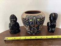 Front view of pottery vase with two obsidian statues on each side, ruler included for scale showing approximately 5 inches height on the statues.