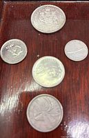 Five Canadian coins on a wooden surface including a 50 cent piece, nickel, two quarters, and a dime showing front designs