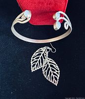 Photo showing the silver-toned cuff bracelet with two moonstone cabochons and the leaf-shaped silver-toned earrings on black background with a red jewelry stand.