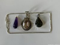 Clear top-down photo of sterling silver chain with three pendants laid out on flat neutral surface. Visible chain clasp and pendant details shown.