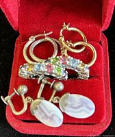 Group photo of four pairs of earrings laid in red velvet box including two silver hoop pairs, colorful stone encrusted hoops and agate clip-ons.