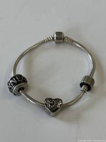 Full view of sterling silver Pandora-style bracelet with three distinct beads including a heart bead with 'Love' engraving.