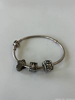 Full view of sterling silver snake chain bracelet with three distinct silver beads including a detailed cross, 'H' letter block, and one decorative bead.