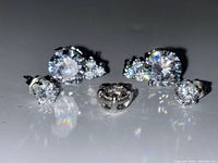 Close-up image showing two pairs of earrings and one pendant laid out on a flat surface. Reflective clear rhinestones set in silver-tone metal.