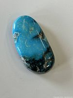 Top view of oblong turquoise cabochon stone showing bright blue color, natural matrix and smooth polished surface.