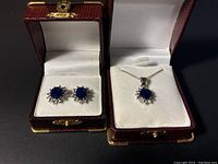 Photo of jewelry set including blue gemstone stud earrings and matching pendant necklace in open jewelry boxes.