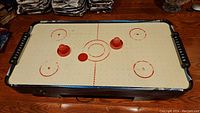 Top view of the air hockey game table showing the playing surface, two red strikers, and puck.
