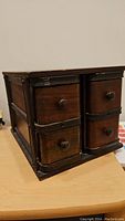 Left angled front view showing antique wood organizer cabinet with four drawers and dark metal corner reinforcements on wooden surface.