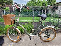 Side profile of olive green folding bicycle showing frame, basket, saddle and rack