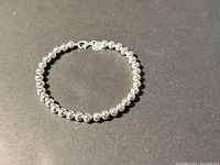 Full view of silver-tone beaded bracelet arranged in circle, showing lobster clasp.