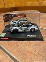 Clear plastic display case with BMW M4 DTM car in white with black and colorful sponsor decals, on a black base labeled with car and driver name.