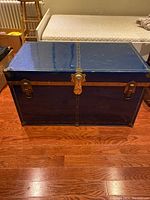 Front view showing blue metal trunk with brass lock and hinges.