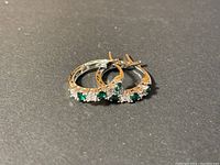 Front view of earrings showing the alternating green and clear stones set in metal hoops on a dark background.