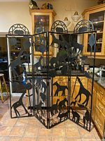 Full view of the four panel black metal divider screen depicting various animal silhouettes in an animal motif, standing open in a kitchen