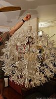 Photo showing the full white pendant light hanging, held up by hand for size reference, displaying radial petal-like white fragments and central spherical frame.
