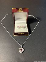 Front view of necklace with heart-shaped pink stone pendant and matching earrings in display box